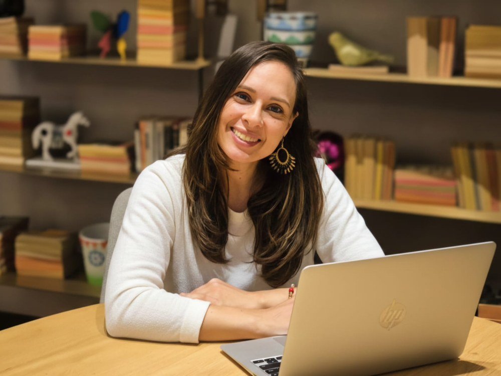 Paula Ledesma sonriendo frente a su computador portátil, con una estantería de fondo